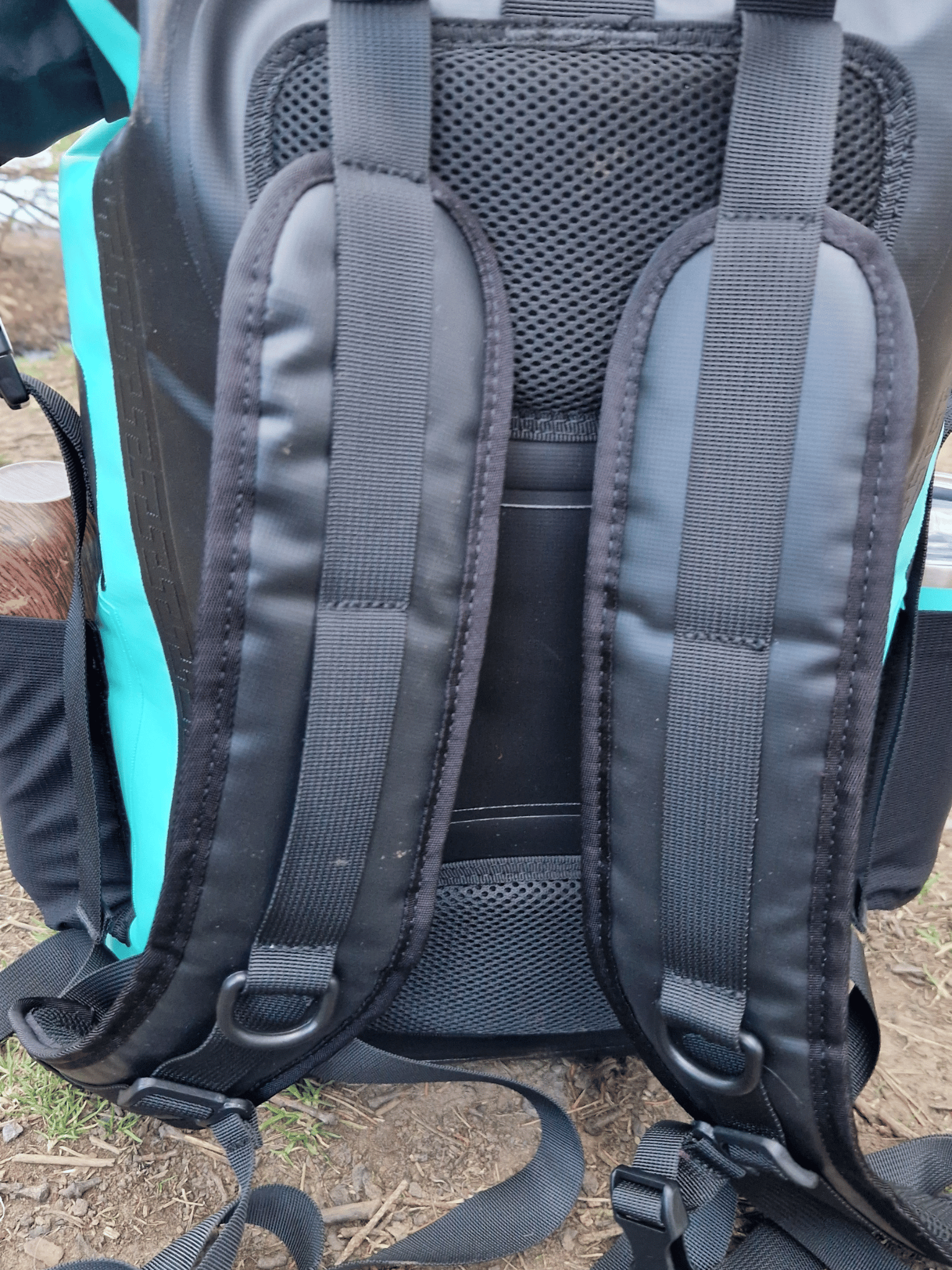 photo of the back of a mint green coloured waterproof bag, showing the padded area and the carrying straps