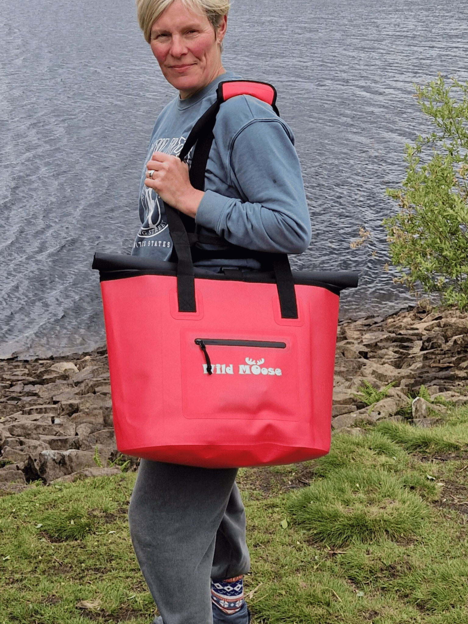 lady with a coral coloured Wild Moose tote bag over her shoulder and next to water