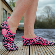 Pink and black leopard print neoprene beach shoes worn by a person on a wooden deck.