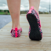 Pink and black patterned neoprene beach shoes on a wooden deck with a blurred natural background