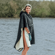Image of woman wearing weatherproof black robe with large front pocket, side popper fastening, hood and white fleece lining