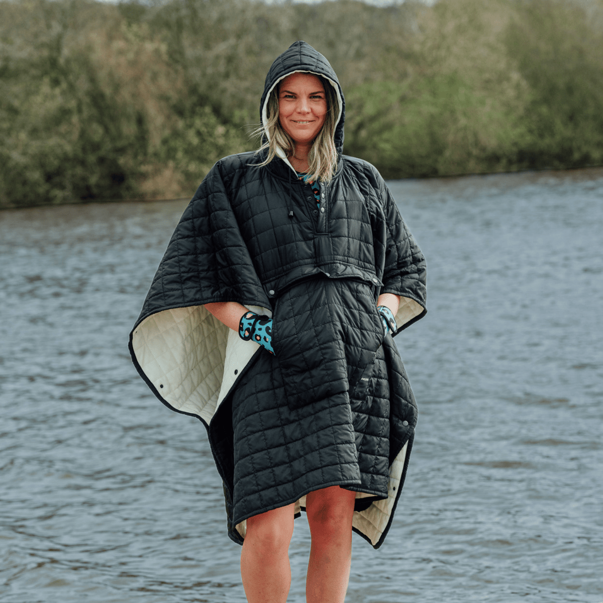 Image of woman wearing weatherproof black robe with large front pocket, side popper fastening, hood and white fleece lining