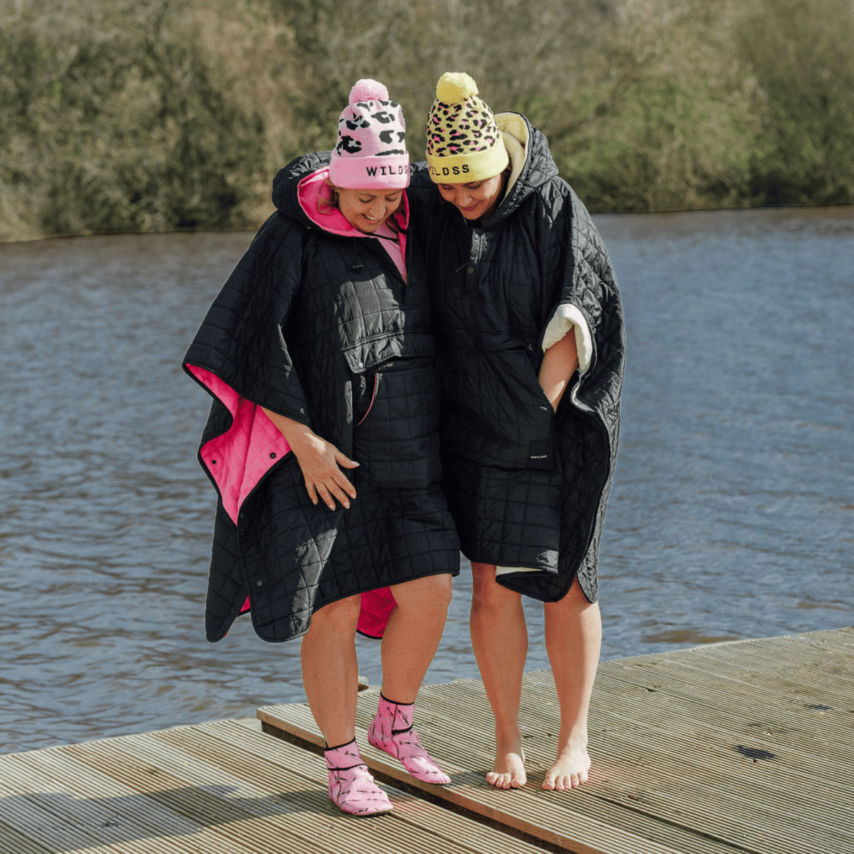Image of 2 women wearing weatherproof black robes with large front pocket, side popper fastening, hood and fleece lining