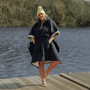 Image of woman wearing weatherproof black robe with large front pocket, side popper fastening, hood and white fleece lining