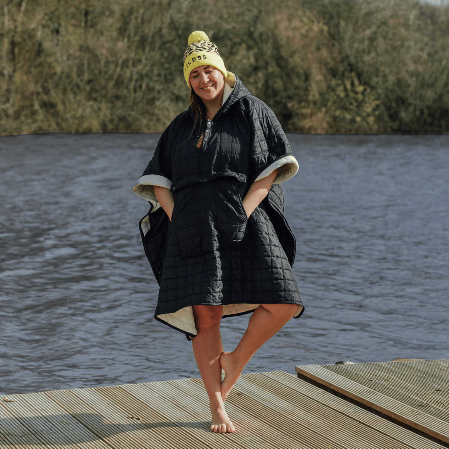 Image of woman wearing weatherproof black robe with large front pocket, side popper fastening, hood and white fleece lining