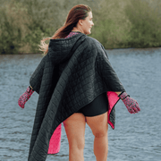 Image of woman wearing weatherproof black robe with large front pocket, side popper fastening, hood and pink fleece lining
