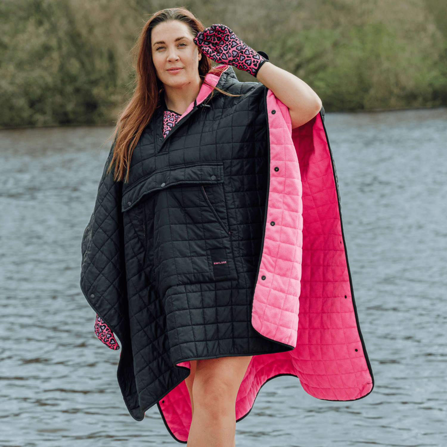 Image of woman wearing weatherproof black robe with large front pocket, side popper fastening, hood and pink fleece lining