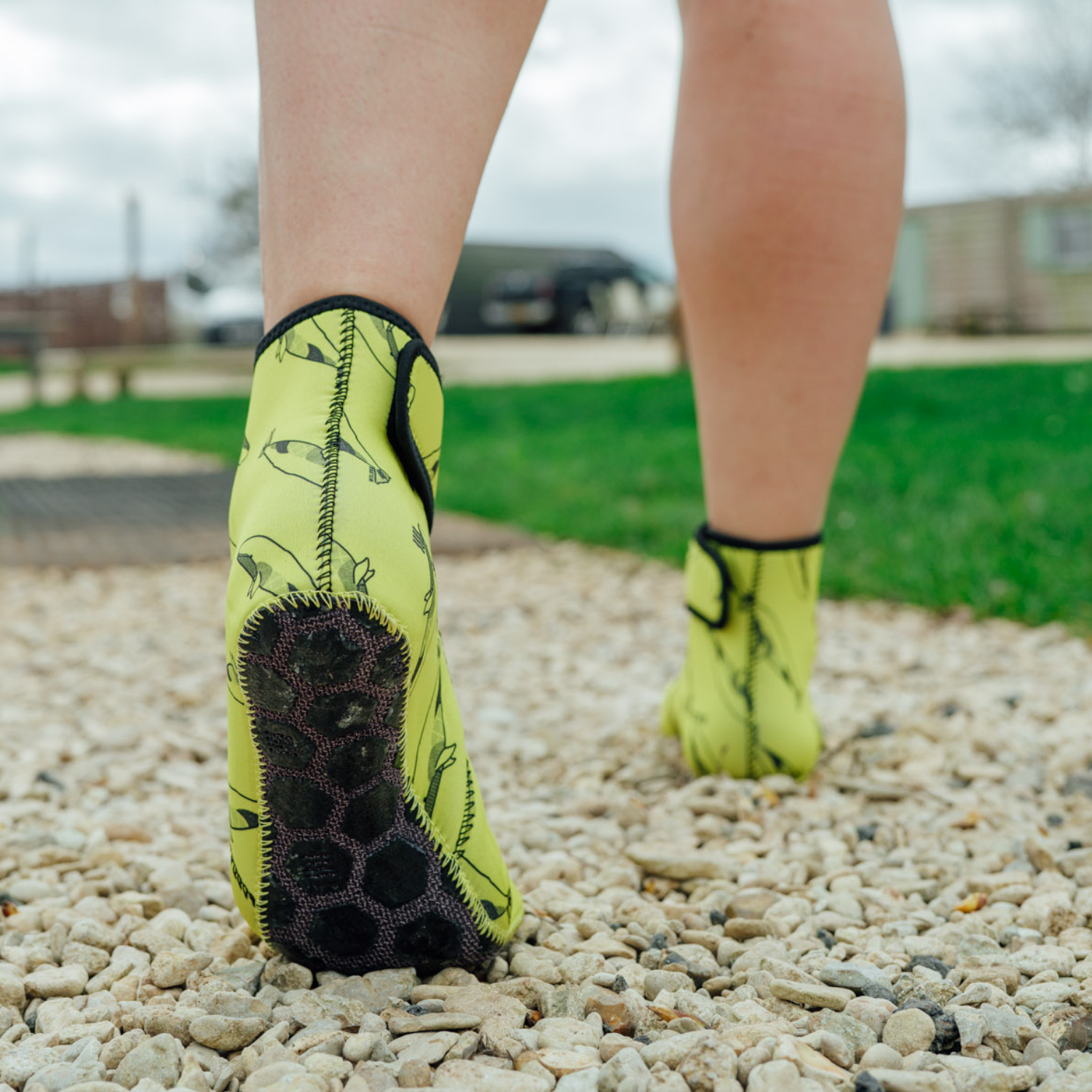 Person wearing bright yellow neoprene socks with black patterns on a gravel surface.