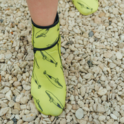 Yellow neoprene swimming boots with black whale pattern on a gravel surface
