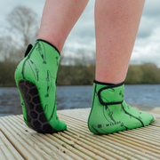 Green neoprene beach socks with black sole design on a wooden dock by a body of water.