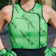 Person wearing bright green neoprene body warmer with black whale patterns, stood by a body of water.