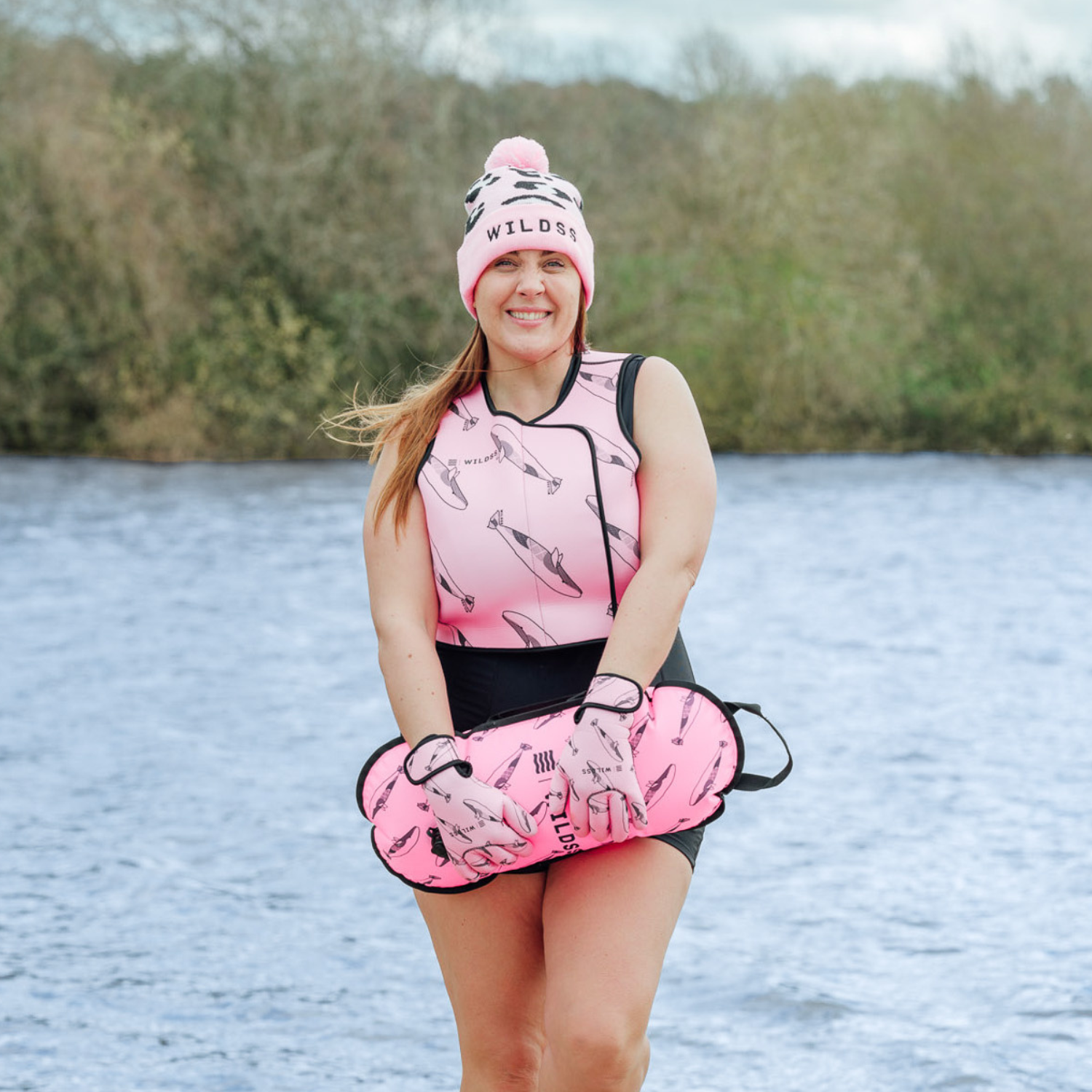 Woman wearing a pink neoprene body warmer  and beanie by a body of water