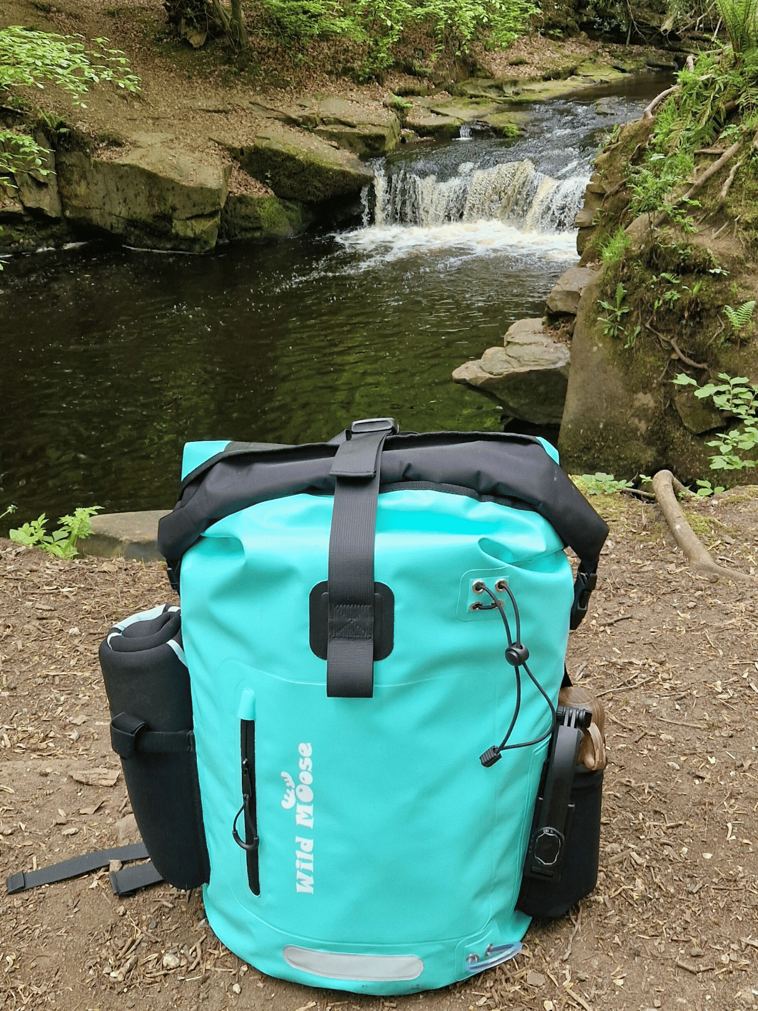 mint green coloured waterproof bag  in the foreground with a small waterfall in the background
