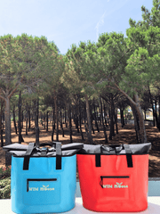 product shot  a bright blue and a coral coloured tote bag with Wild Moose logo on a white wall in front of a pine forest