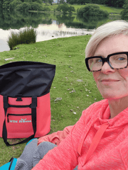 lady sat at the edge of a tarn with  a coral coloured Wild Moose tote bag open 