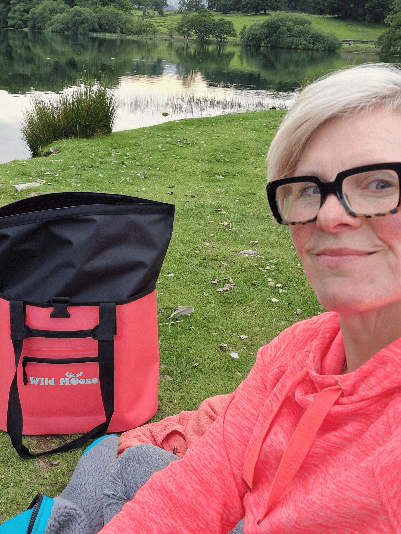 lady sat at the edge of a tarn with  a coral coloured Wild Moose tote bag open 