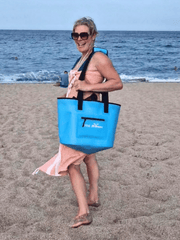 lady stood on a beach, laughing and carrying a bright blue tote bag